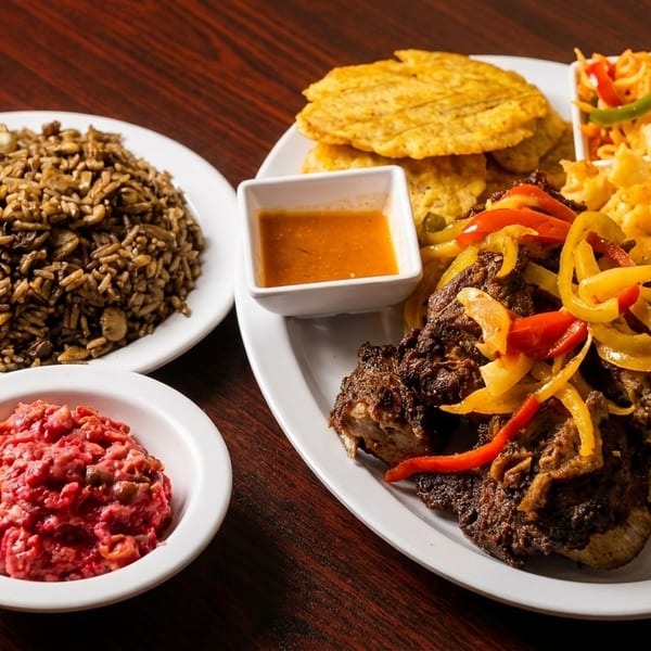 A large plate of Caribbean food with rice, meat, plantains, and a side of red salad.