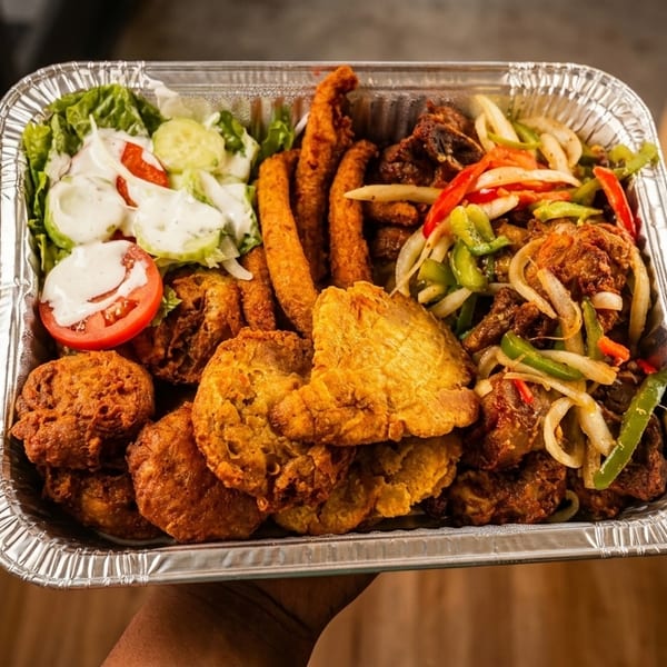 A large foil tray filled with fried chicken, plantains, salad, and sautéed vegetables.