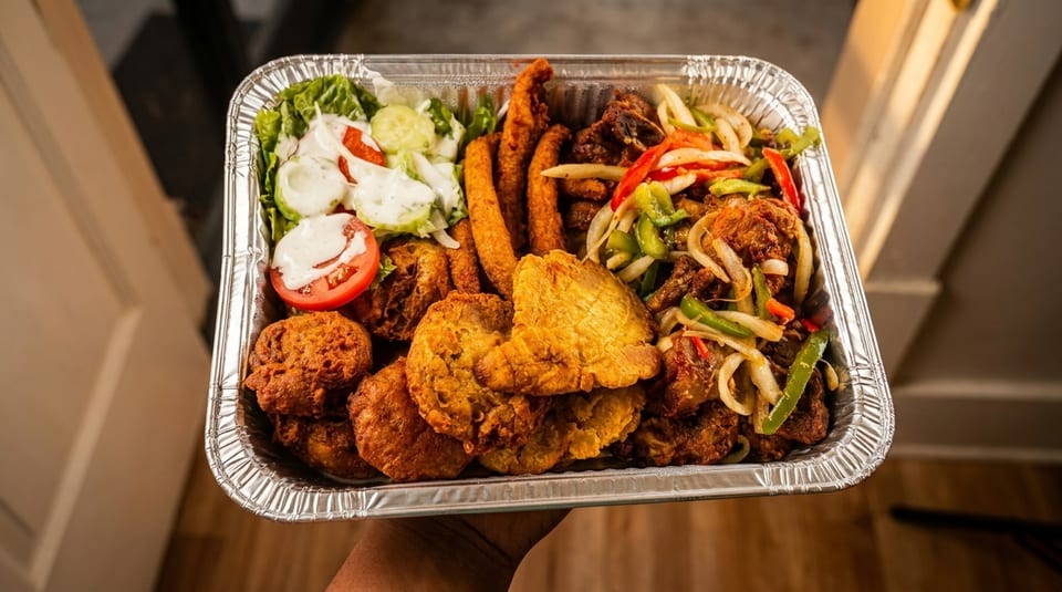 A large foil tray filled with fried chicken, plantains, salad, and sautéed vegetables.