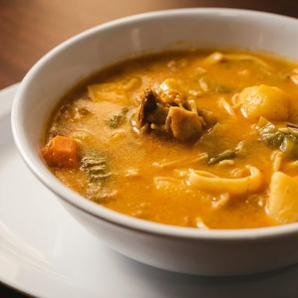 Hearty chicken noodle soup with vegetables in a white bowl on a wooden table.