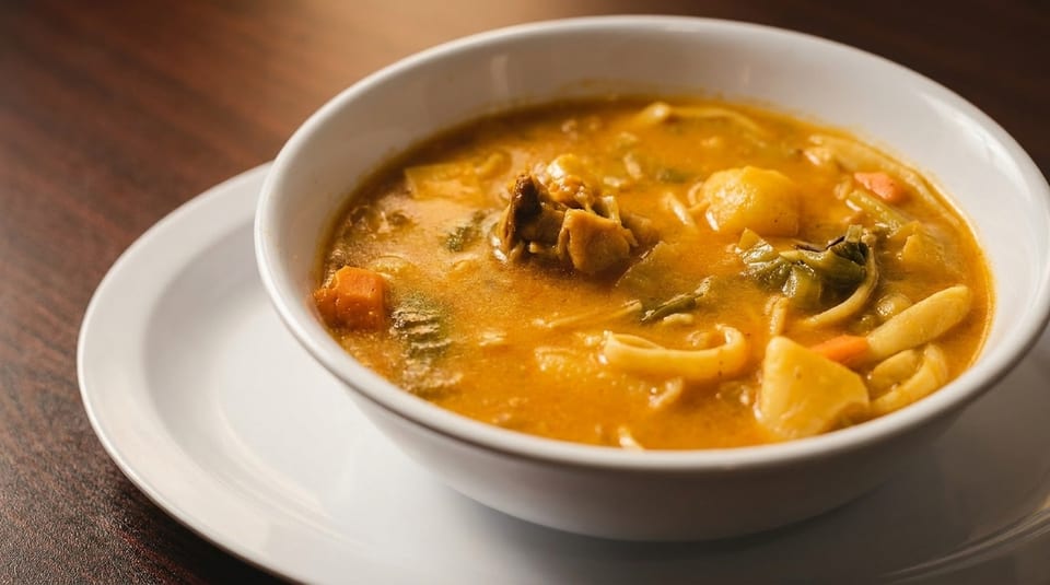 Hearty chicken noodle soup with vegetables in a white bowl on a wooden table.