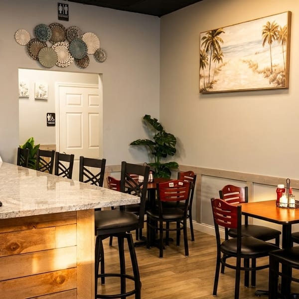 Restaurant interior with a counter, bar stools, dining tables, chairs, and wall decor.